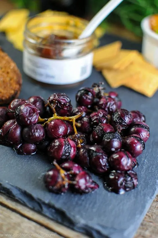 Grapes, jar of jam with white spoon, crackers on slate