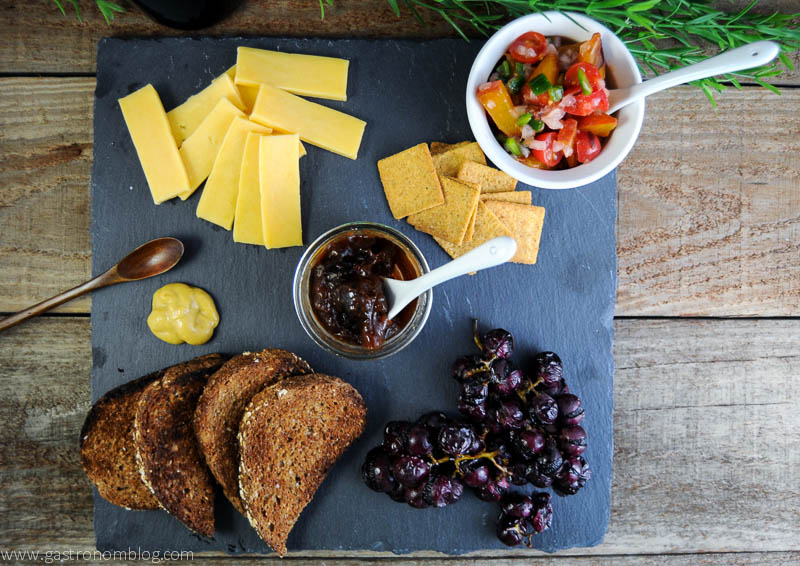 Roasted grapes on a charcuterie plate with salsa, cheese, crackers, jam and toast