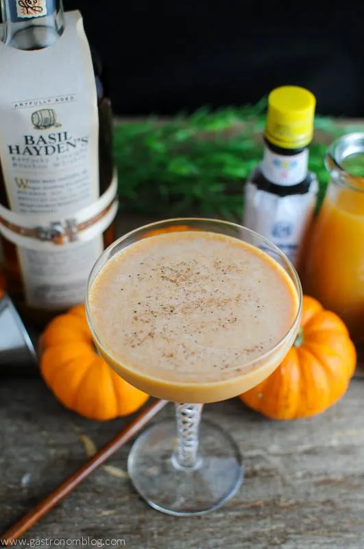 Orange creamy cocktail in coupe, pumpkins, wooden spoon and bottle behind
