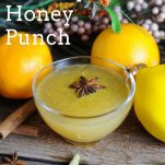 Yellow whiskey punch recipe in punch cups with star anise. Spices and oranges behind with flowers.