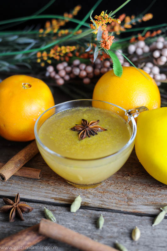 Yellow whiskey punch recipe in punch cups with star anise. Spices and oranges behind with flowers.