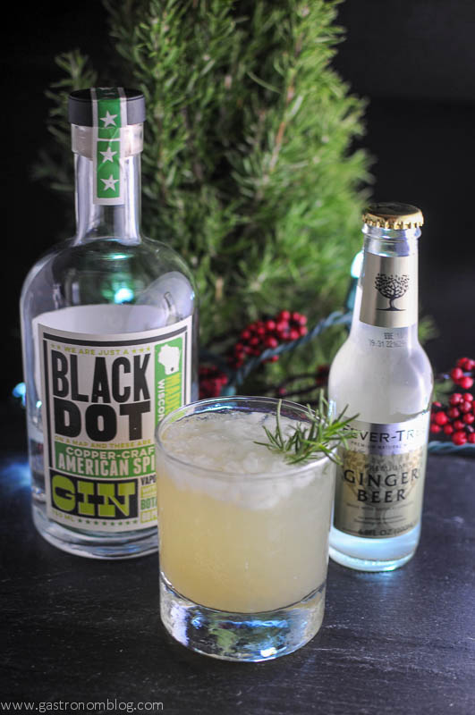 Rosemary's Pear cocktail in a rocks glass with gin bottle and ginger beer bottle with tree in background