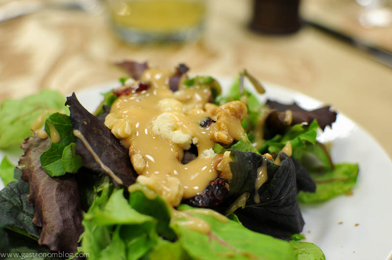 Mixed greens on a white plate, cashews and yellow dressing