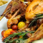 Whole roast turkey on white platter with roast veggies and rosemary