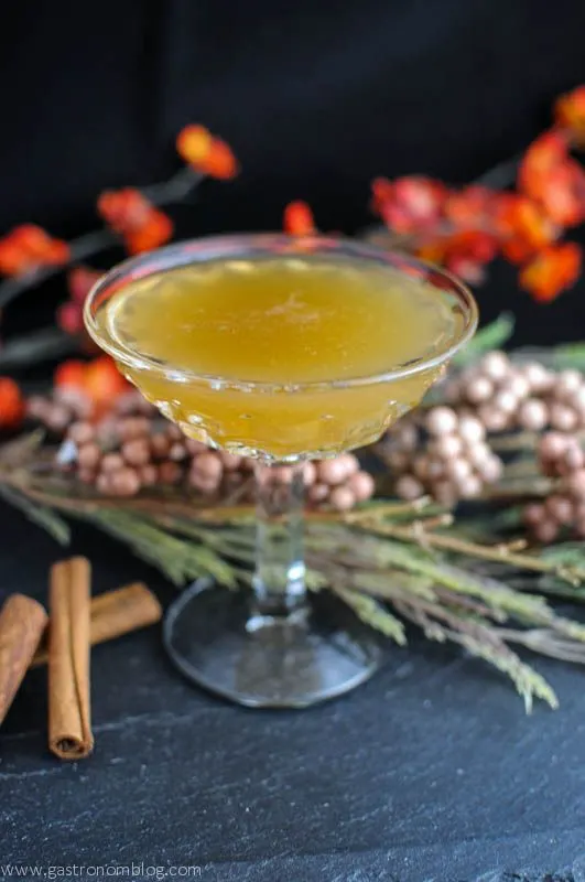 Whiskey Lush Cocktail- golden cocktail in coupe. Cinnamon sticks and flowers in background