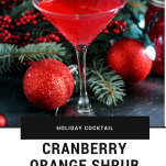 Cranberry Orange Shrub Cocktail - red cocktail in martini glass with sugared cranberries on pick. Evergreen and Christmas ornaments in background