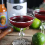 Purple cocktail in coupe, vodka bottle and limes