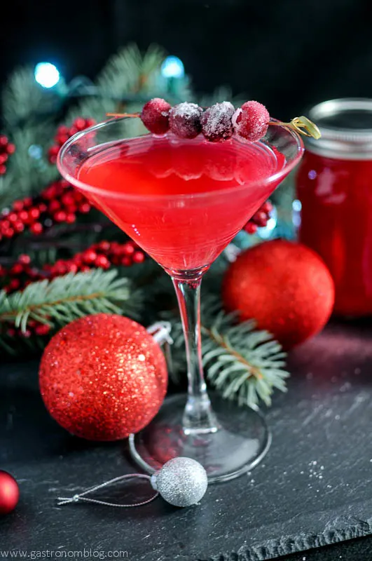 Cranberry Orange Shrub Cocktail - red cocktail in martini glass with sugared cranberries on cocktail pick, greenery and christmas ornaments in background