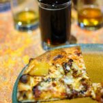 Pizza on green rimmed plate with dark beer in glass behind