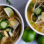 Pho soup in white bowls with limes and sprouts on top