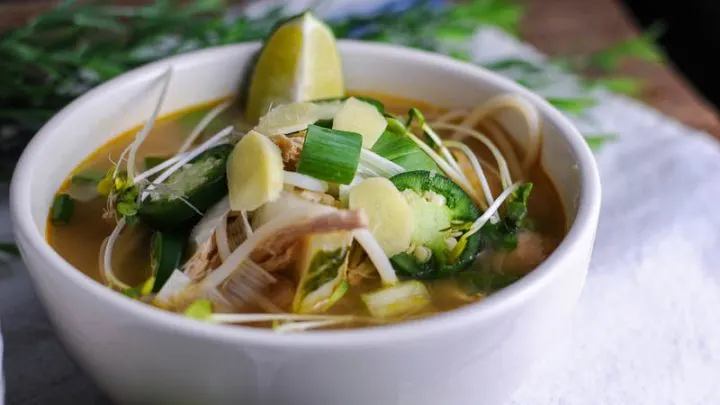 Chicken Pho in a white bowl on a white napkin. Topped with jalapeno and lime slices