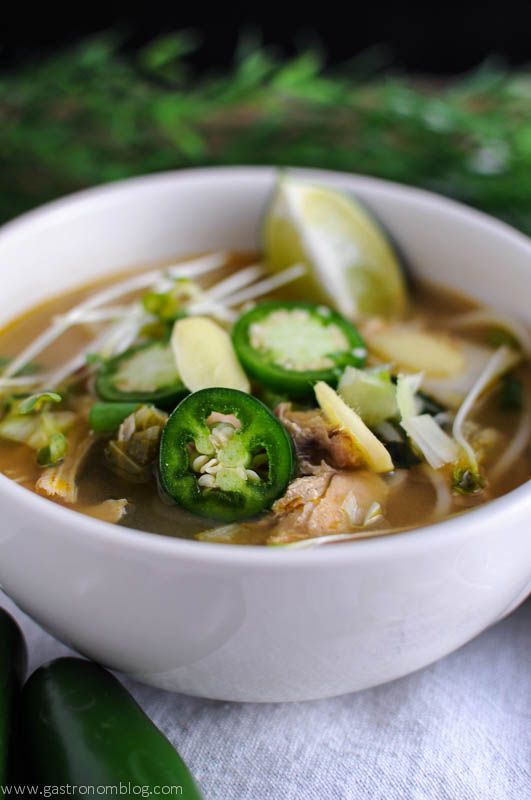 Slow Cooker Chicken Pho soup in white bowls topped with lime wedges, jalapeno slices, and more, limes and jalapenos next to bowls on white napkin