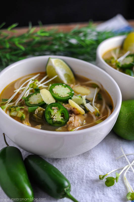 Crockpot Pho in two bowls, jalapenos, limes and sprouts on a white napkin. Slowcooker pho
