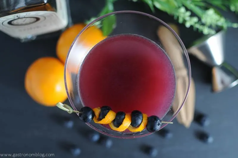 Garnet cocktail in a martini glass with oranges, jigger, reamer and vodka bottle in the background