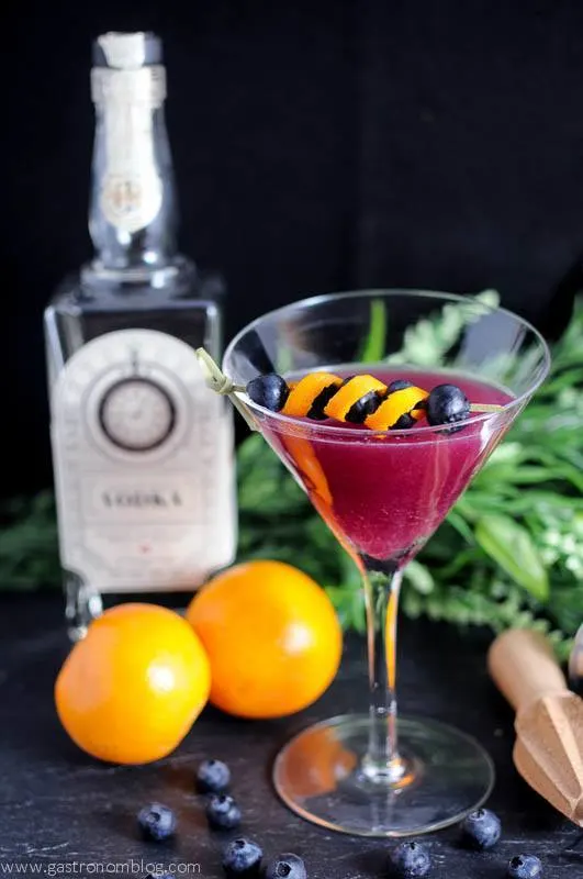 Garnet Martini in a martini glass, gin bottle behind, oranges and greenery