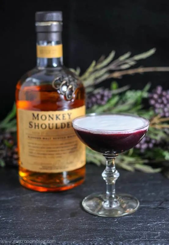 The Black Scot cocktail in a cocktail coupe, Monkey Shoulder whisky bottle and flowers in background for this scotch cocktail