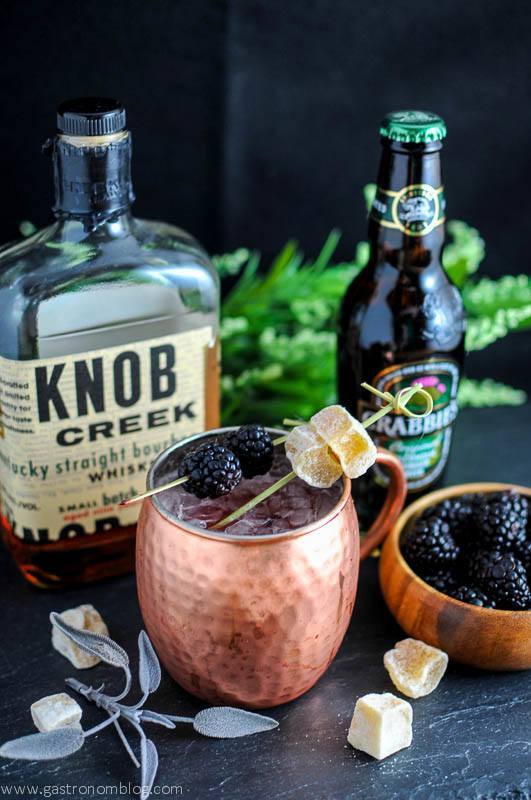 Mule in copper cups with blackberries and ginger on picks. Bourbon bottle and ginger beer bottle with flowers behind