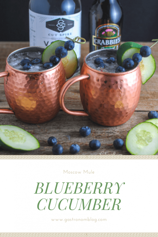 Blueberry Cucumber Moscow Mules in copper mugs with cucumbers and blueberries. Vodka and Ginger beer bottles in back.