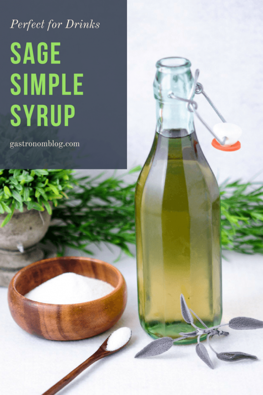 Sage Simple Syrup - green syrup in tall bottle. Wooden bowl and spoon with sugar and sage leaves next to bottle. Greenery behind