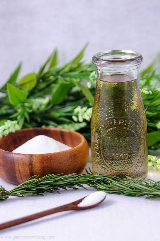 Green Rosemary simple syrup in a jar, wood bowl of sugar, green floral behind