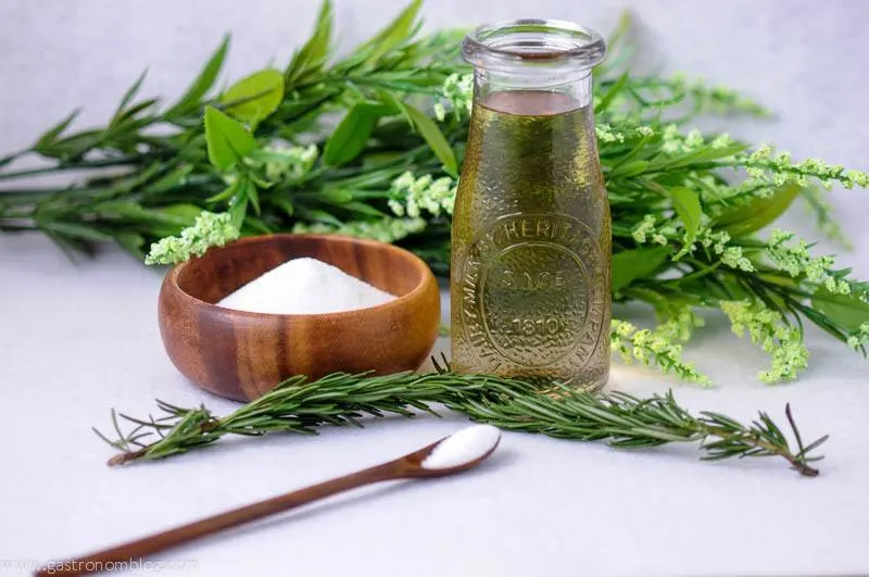 Green Rosemary simple syrup in a jar, wood bowl of sugar, green floral behind