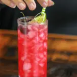 Bright pink cocktail in highball with green straw, lime and cherries