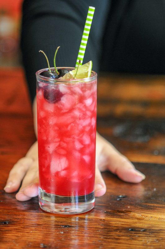 Ginger Cherry Smash Cocktail in a highball glass with a lime and cherries