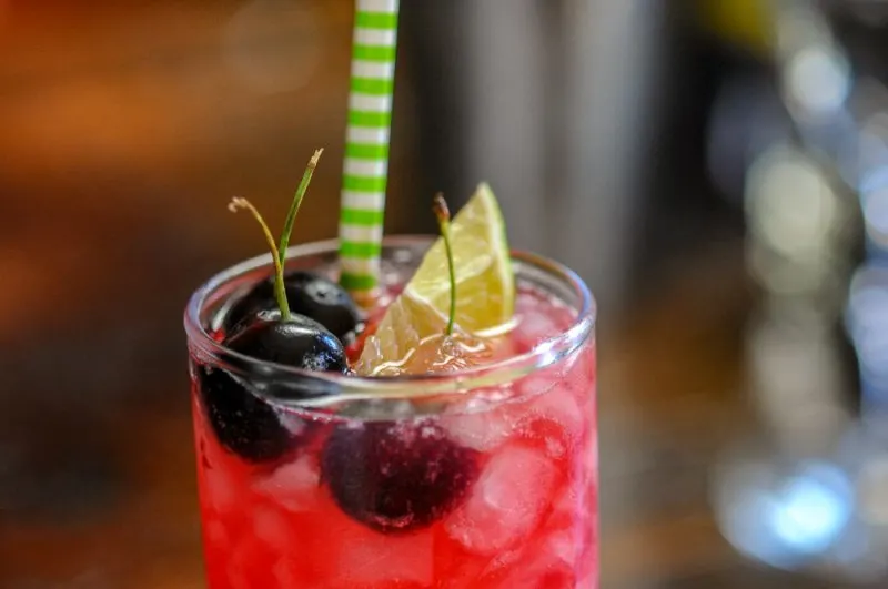 Ginger Cherry Smash Cocktail in a highball with a green and white straw