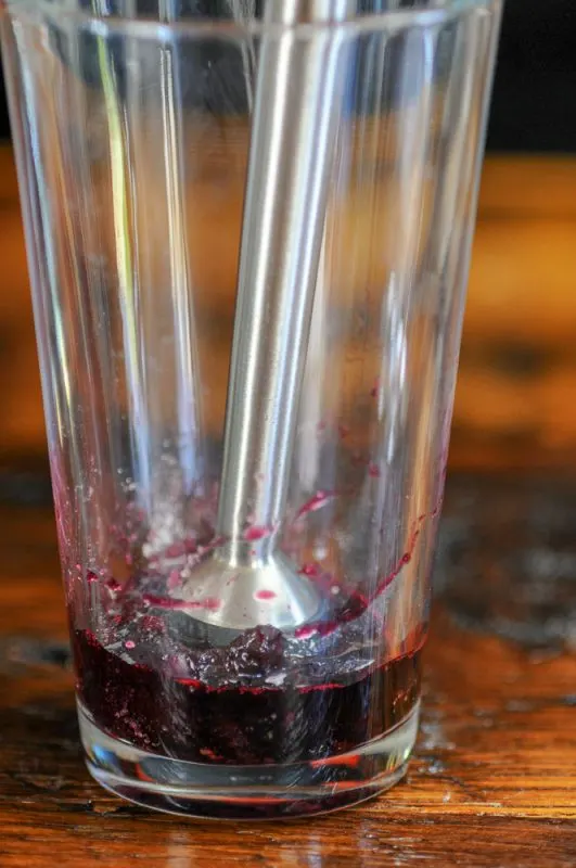 Cherries being muddled in a glass