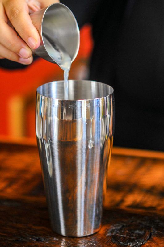 Lime juice being poured from a jigger into a shaker