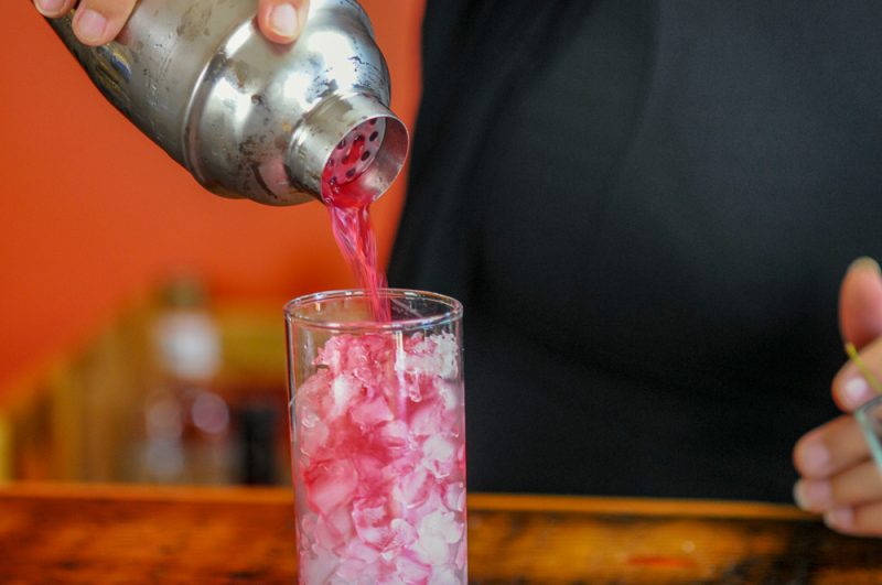 Ginger Cherry Smash Cocktail - pink cocktail being poured from shaker into highball glass filled with ice