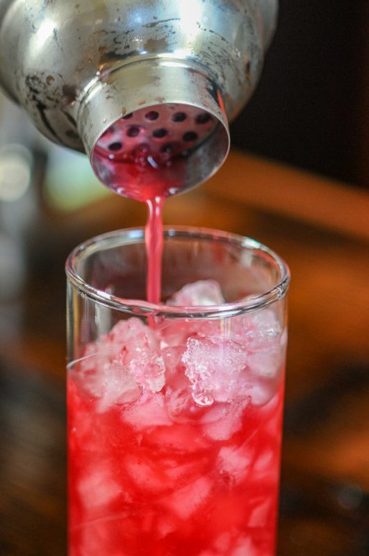 Ginger Cherry Smash Cocktail, pink cocktail being poured in an ice filled highball