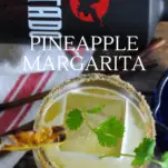 Top shot of yellow cocktail in glass with cilantro on ice, bottle of tequila