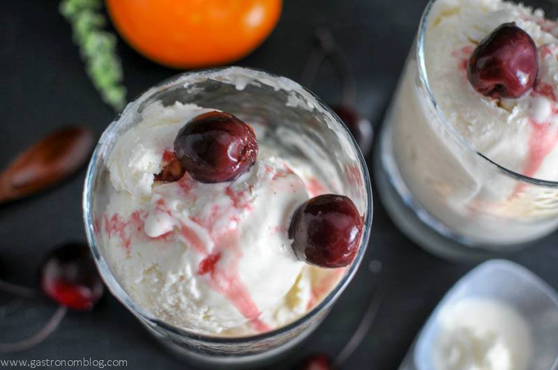 No Churn Old Fashioned Ice Cream in rock glasses with brandied cherries on top and in a jar. Orange, wooden spoons and cherries on slate board