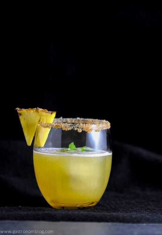 Pina de Fuego Cocktail, yellow drink with pineapple slice on a black background