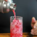 Bright pink cocktail being poured into highball glass