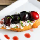 Cherries and goat cheese on top of bread on white plate