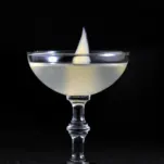 White colored cocktail in coupe with ginger slice