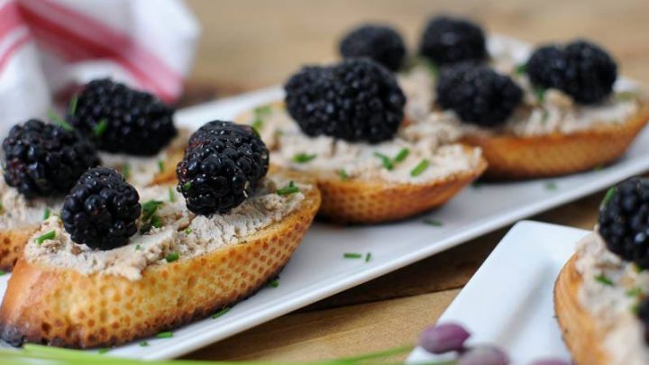 Toasted bread on white plate. Blackberries on top of toasts. Chives and napkin in background