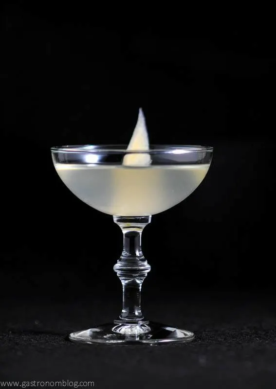 sake cocktail in coupe with slice of pickled ginger in front of black background