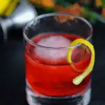 Red cocktail in rocks glass, lemon peel