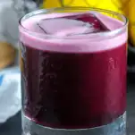 Purple cocktail in glass with foam on top, lemons in background