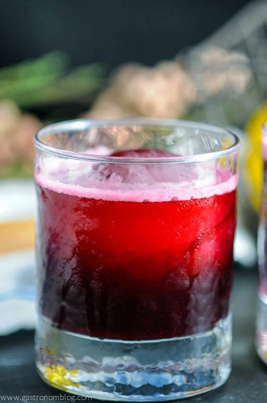 The Aronia Sour cocktail in a rocks glass with reamer, white napkin, flowers and wire basket in background