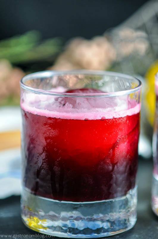 Red cocktail in rocks glass with ice ball. Flowers in background