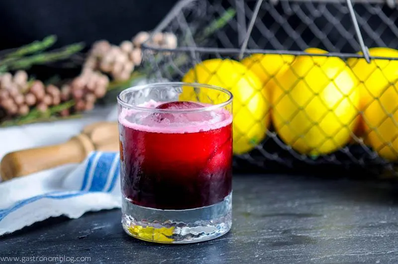 Bourbon Candied Pecans - cinnamon, brown sugar, sugar, vanilla, egg white, honey, bourbon, nutmeg, cloves, pecans, salt from Gastronomblog. #bourbon #whiskey #gastronomblog #sugar #NewOrleans The Aronia Sour cocktail in a rocks glass with reamer, white napkin, flowers and wire basket in background