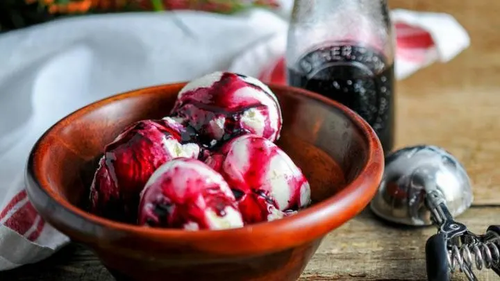 Aronia Berry Syrup - purple syrup on ice cream in wooden bowl. Purple syrup in glass jar behind