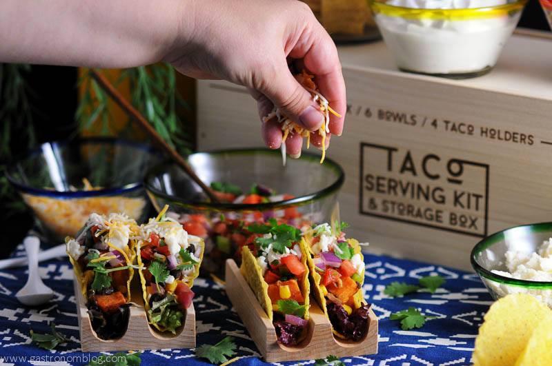 Sweet potato, black bean and corn tacos in wooden stands with glass bowls and wooden box in background