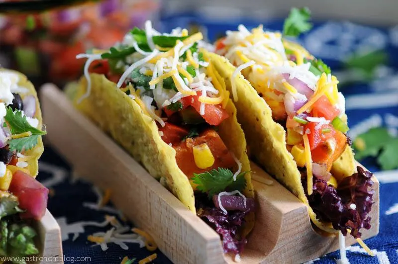 Sweet potato, black bean and corn tacos in wooden holder on blue and white napkin