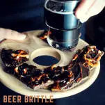 Beer Brittle Chocolate Bark pieces on wood tray with hand holding dark beer
