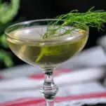 Greenish clear cocktail in coupe with fennel front on white and red napkin
